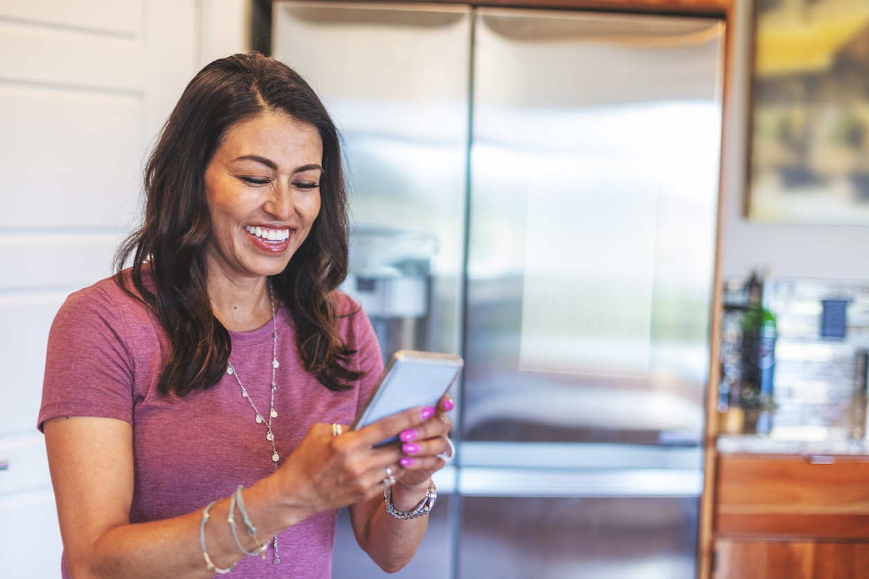 woman smiling at phone and standing in the kitchen  
